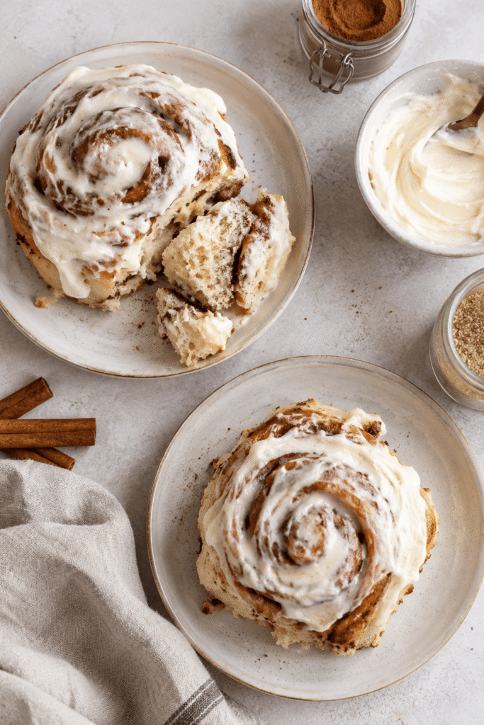 Fluffige Zimtschnecken mit cremigem Frischkäse-Frosting auf hellen Tellern